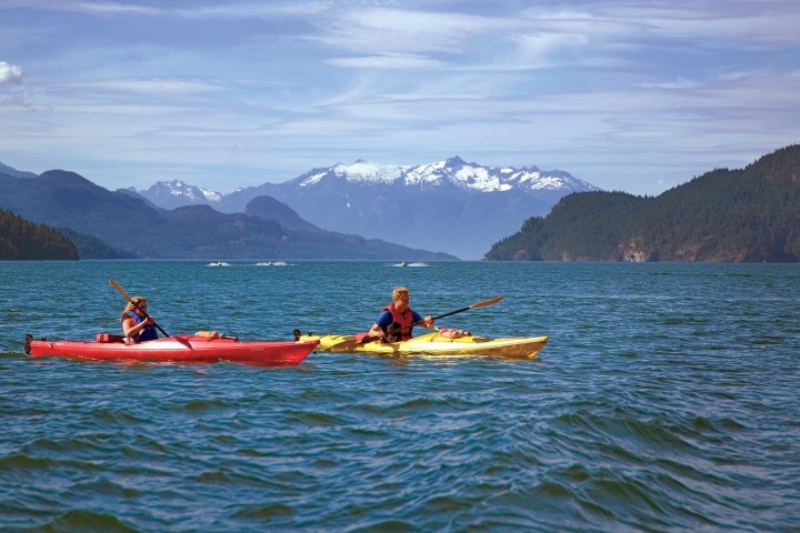 a man and a woman rowing an ocean kayak in a body of water